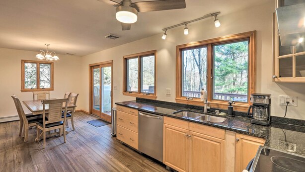 A modern kitchen with wooden cabinets, a dishwasher, a coffee maker, and a large window overlooking a wooded area. - Family-friendly Woodbury Home With Yard + Deck! (Woodbury)
