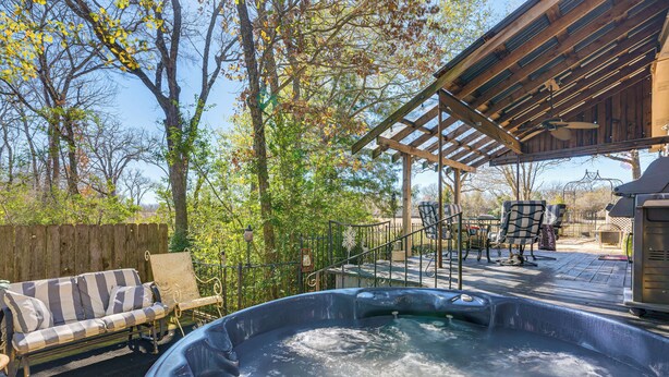 Een hottub met een houten terras, een overdekte zithoek en een omheinde tuin met bomen.