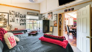 Een gezellige slaapkamer met een bed, een bureau en een stoel. Er is een deur die naar een andere kamer leidt, en een televisie aan de muur bevestigd.