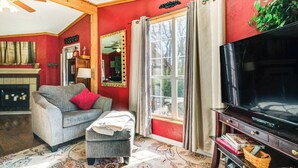 Een woonkamer met een open haard, een bank, een televisie en een groot raam met gordijnen.