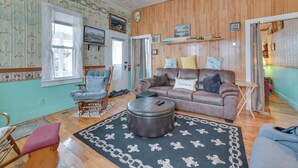 A cozy living room with a brown leather sofa, a round ottoman, and a blue armchair. - Historic Houghton Lake Getaway Near Shoreline (Houghton Lake)