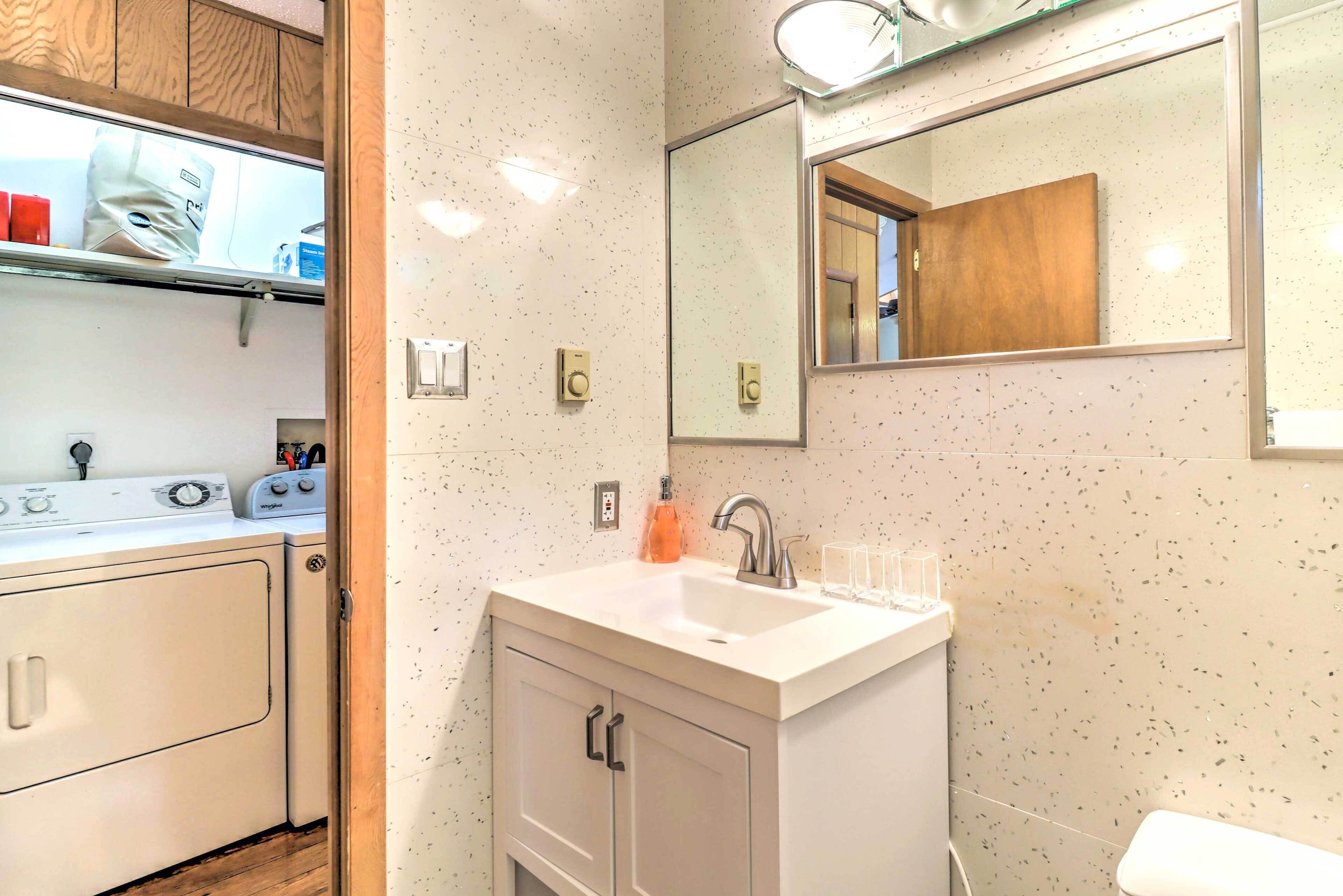Un baño con lavamanos, espejo y lavadora.