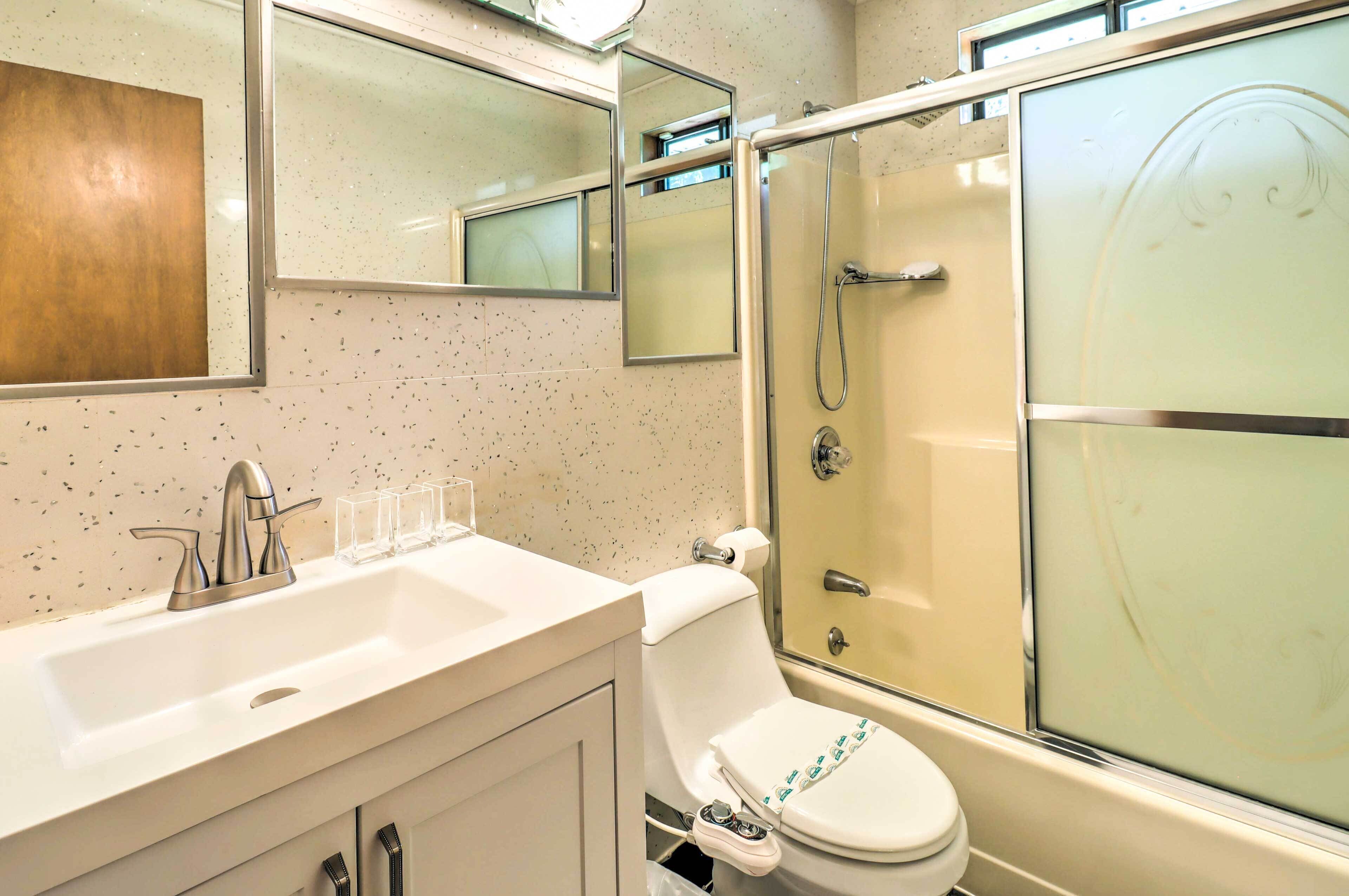 Un baño con lavamanos blanco, inodoro, cabina de ducha de vidrio y espejo sobre el lavamanos.