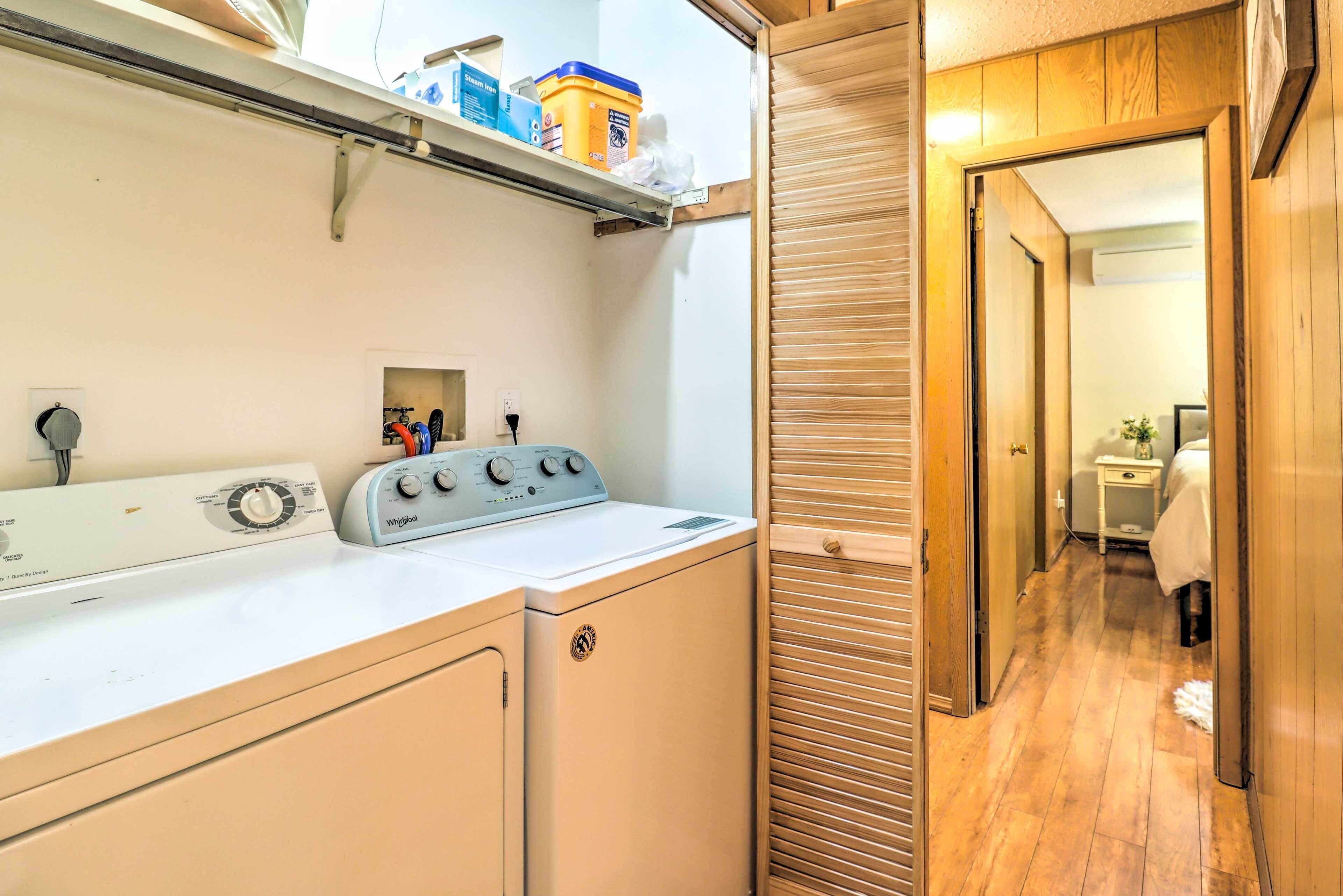 A laundry area with a washer and dryer, a shelf with cleaning supplies, and a wooden door leading to another room.
