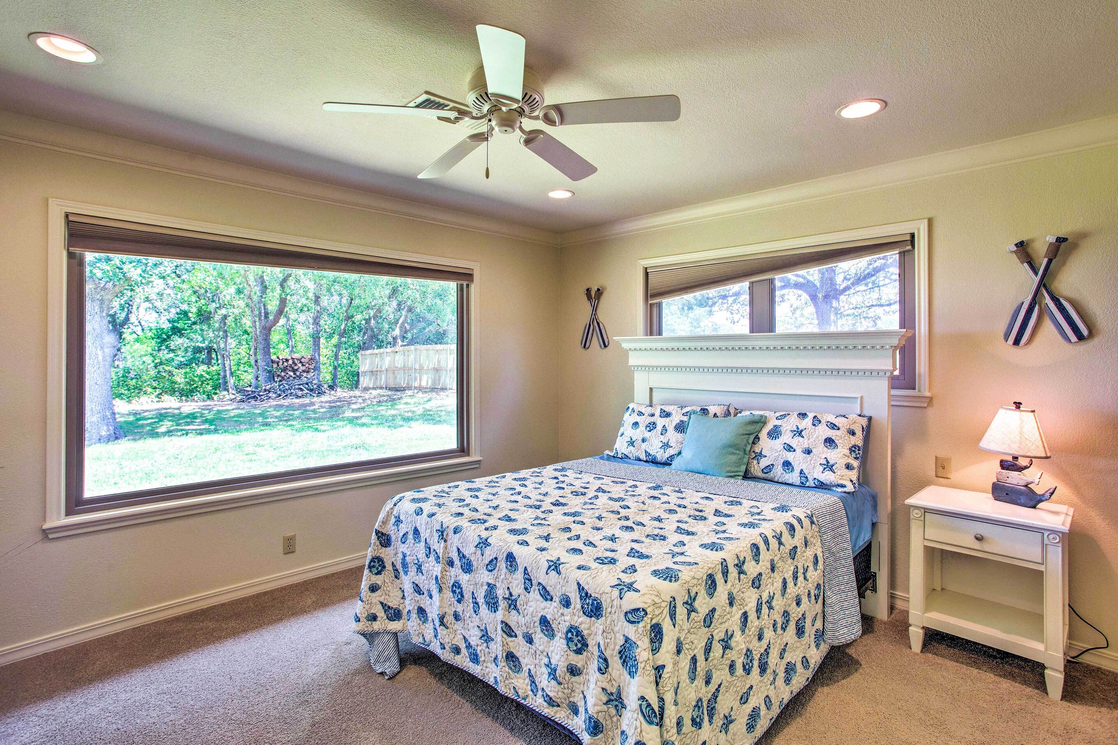 A bedroom with a bed, a nightstand, a ceiling fan, and two windows.