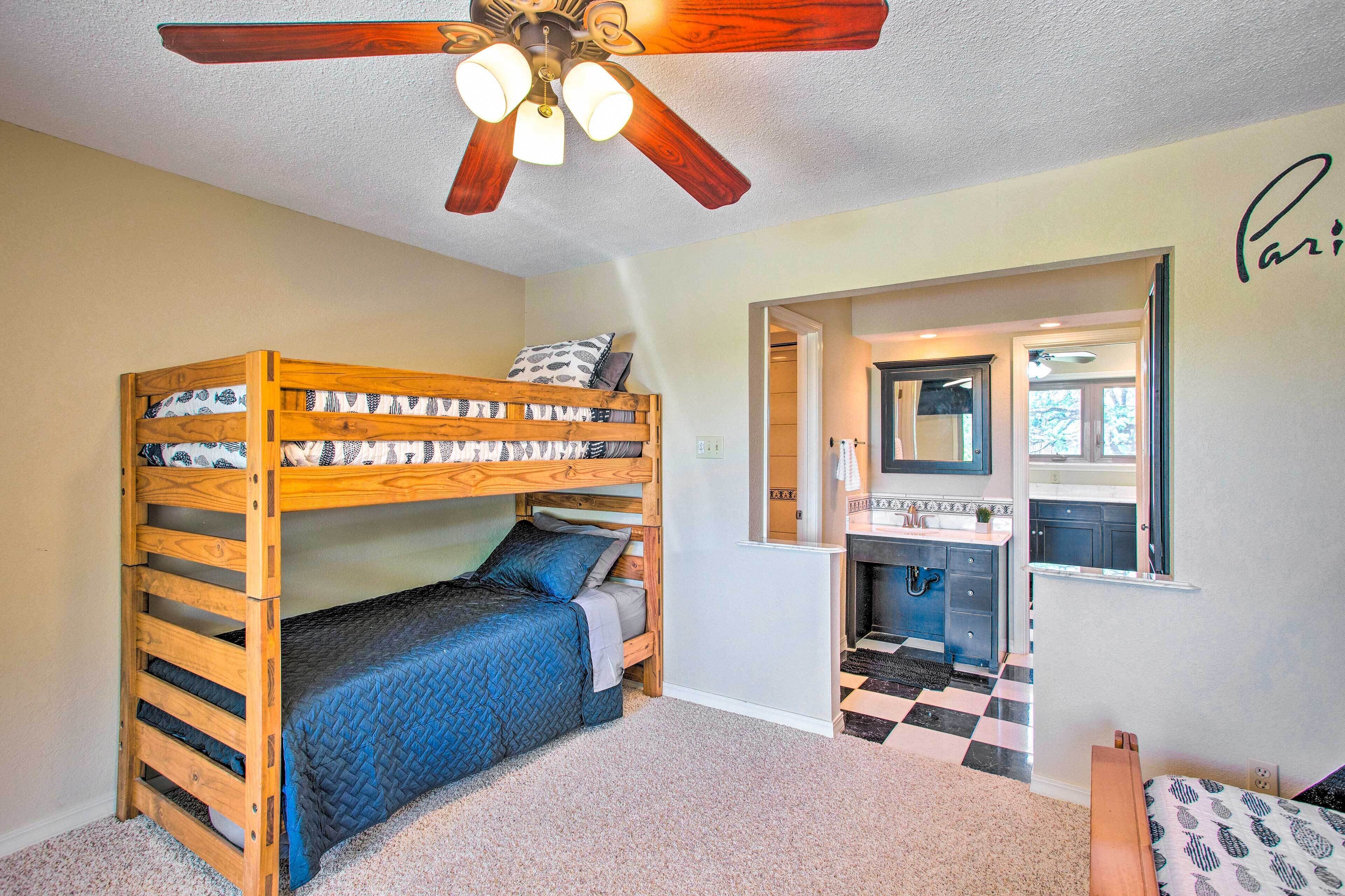 A bedroom with a bunk bed, a ceiling fan, and a view into the bathroom.