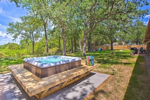 A hot tub on a wooden platform in a backyard with trees and a barbecue area.