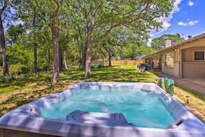 A backyard with a hot tub surrounded by trees, a covered patio, and a brick building.