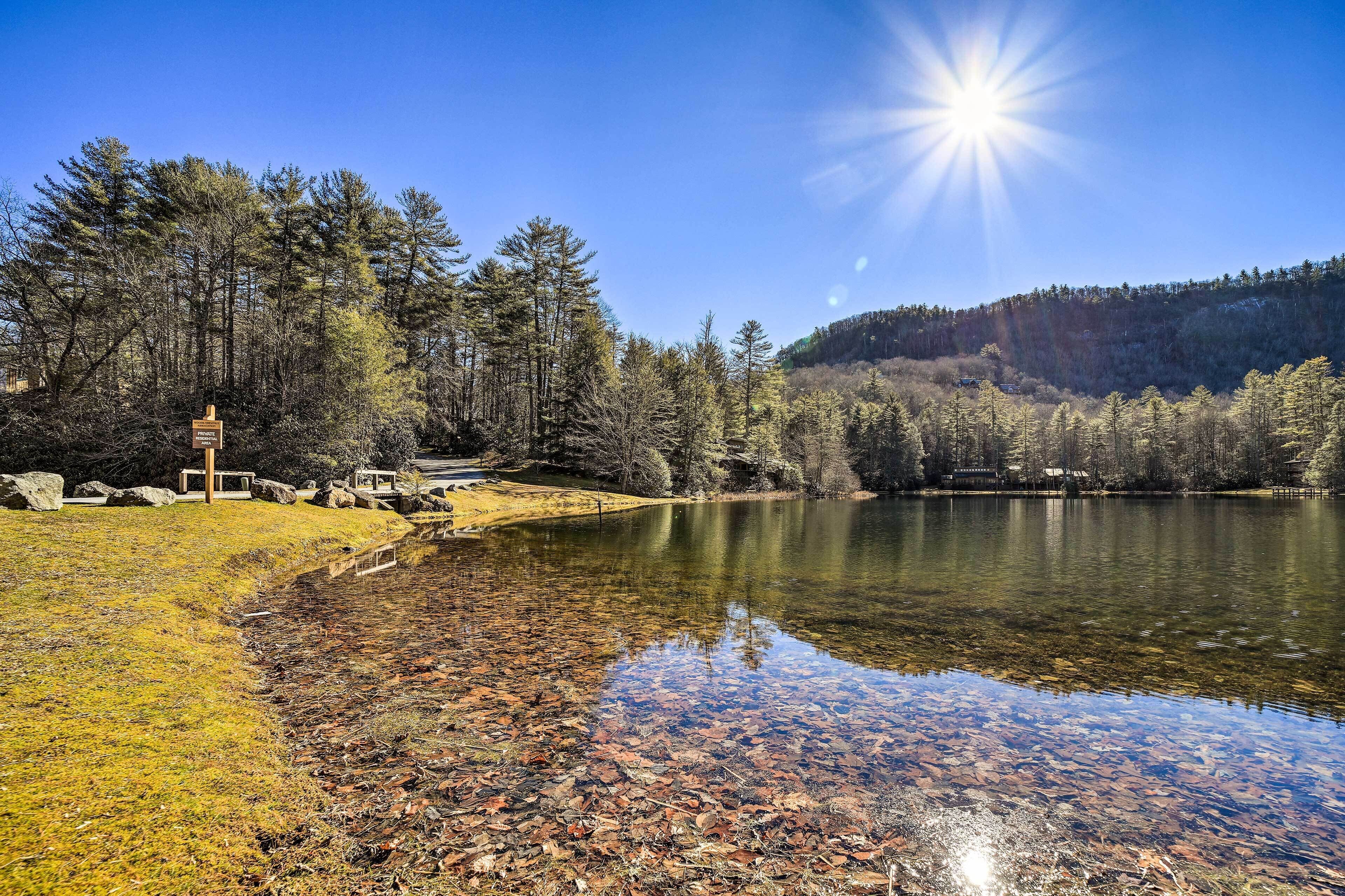 Un lago transparente con orilla rocosa, rodeado de árboles y una colina al fondo.