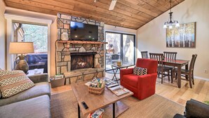 A cozy living room with a stone fireplace, a red armchair, a wooden coffee table, and a dining area with a table and chairs. - Sunny Sapphire Townhome w/ Resort Amenities! (Sapphire)