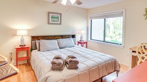 Ein Schlafzimmer mit einem Bett, zwei Nachttischen, einem Fenster und einem Deckenventilator.