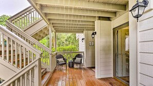 Eine überdachte Veranda mit Holzterrasse, zwei Korbstühle, einem kleinen Tisch und einer Glastür, die zu einer Garage führt.
