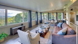 A spacious living room with large windows, a sofa, chairs, a coffee table, and a dining area.