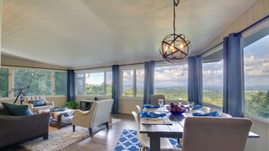 A spacious room with a dining area, large windows offering a scenic view, and a hanging light fixture.