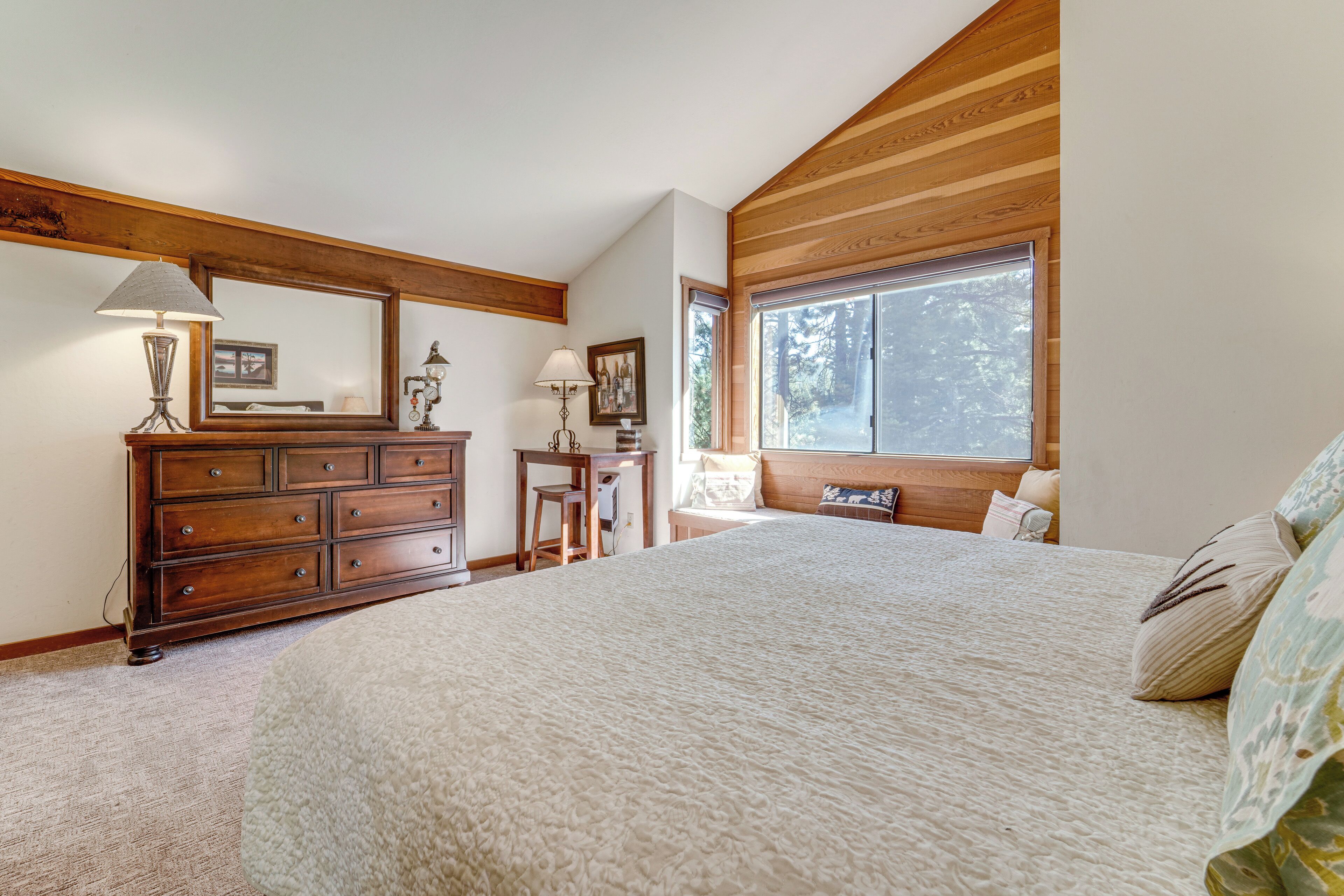 Camera da letto con un letto grande, una cassettiera in legno e una finestra vista alberi.
