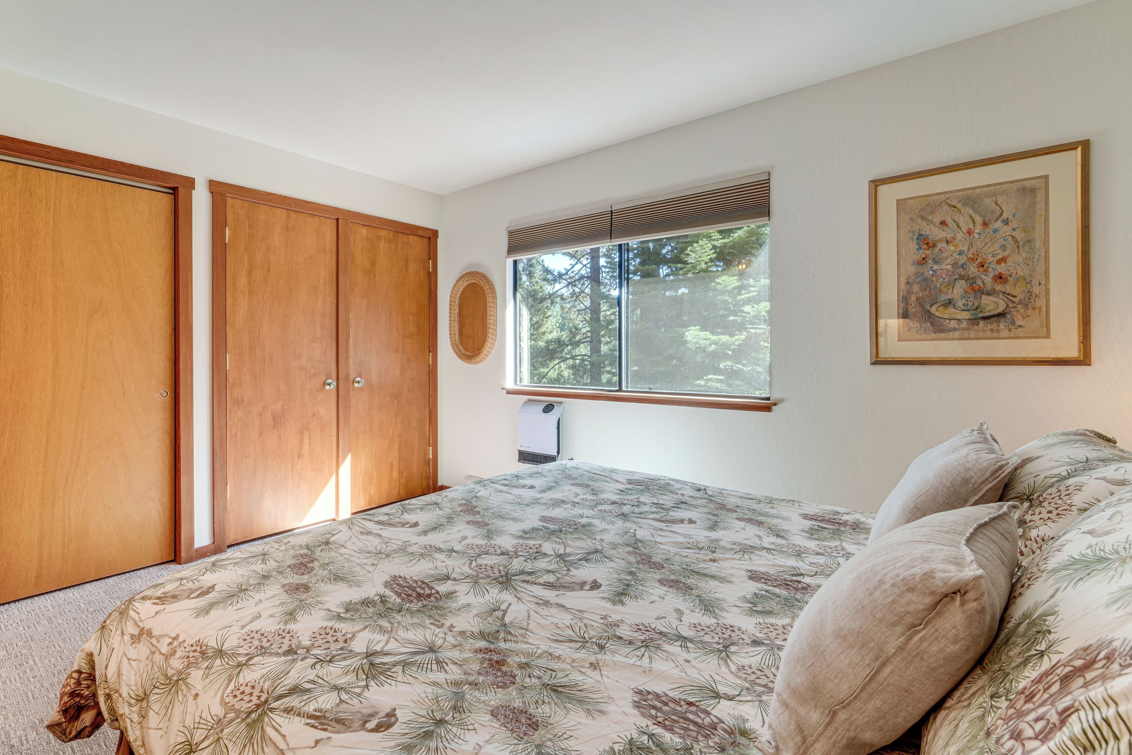 A bedroom with a bed, wooden wardrobe, a window with blinds, and a framed artwork on the wall.