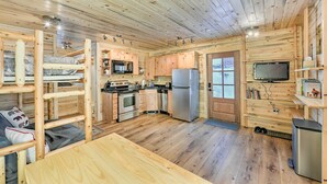 L’intérieur d’une cabane en bois est aménagé avec des lits superposés, un coin cuisine, un téléviseur et un petit réfrigérateur.
