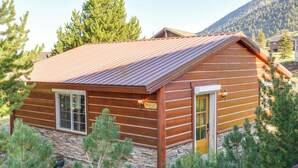 Une cabane en rondins avec un toit en métal, des fondations en pierre et entourée de pins.