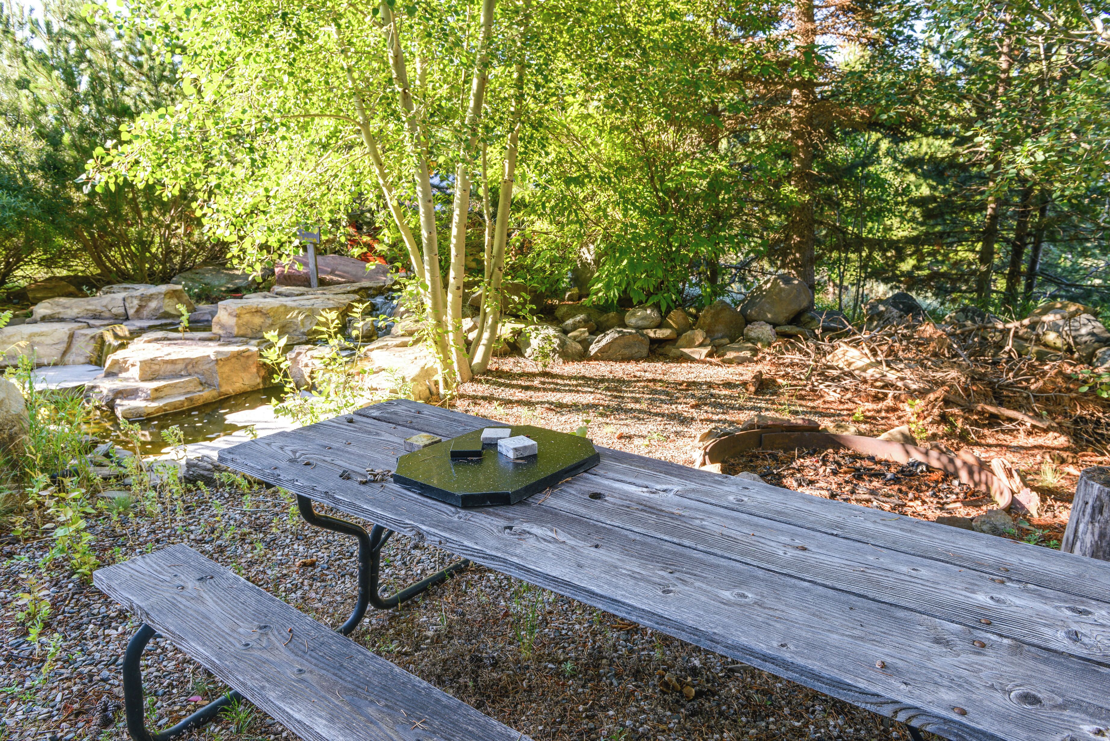 A wooden picnic table with a green tray in a forested area with rocks and trees.