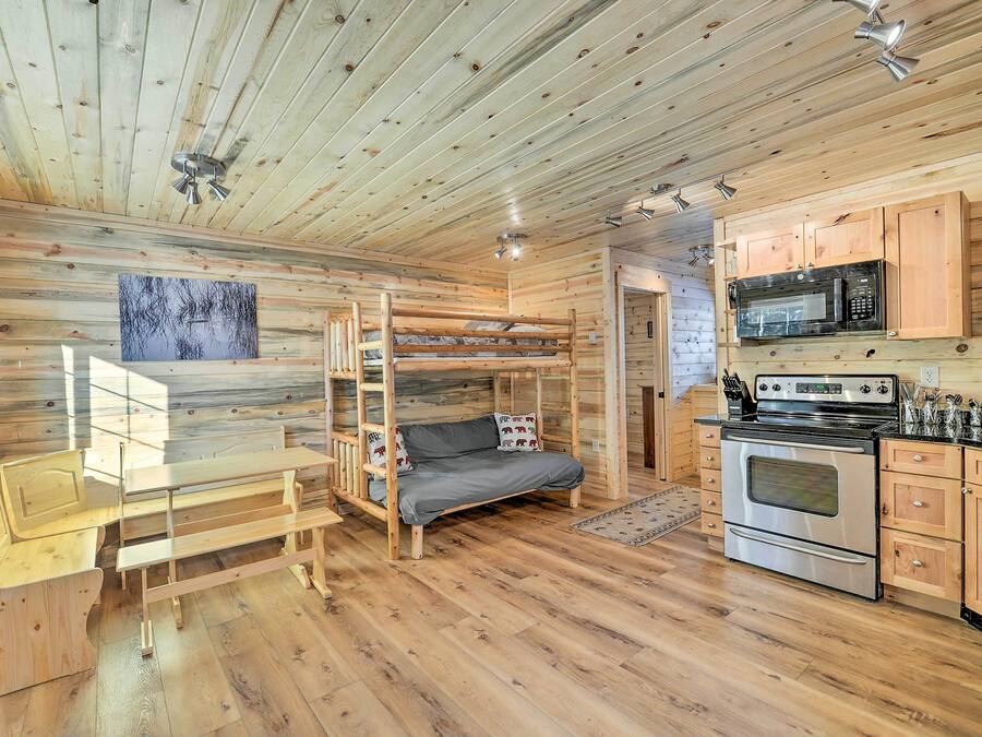 Interior acogedor de una cabaña con literas, una mesa de comedor, un sofá, una zona de cocina con estufa y microondas, y paredes de madera.