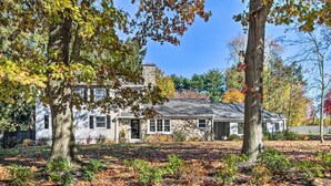 A two-story stone house with a stone chimney, surrounded by trees and a leaf-covered lawn. - 20 Mi to Philly: Inviting Home w/ Yard in Wayne! (Wayne)