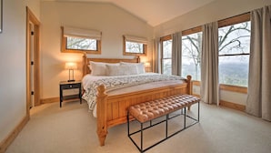 A bedroom with a wooden bed, a bench, a nightstand, and large windows with curtains. - Sapphire 5BR Luxe: 5 Private Baths, Mtn Views (Sapphire)