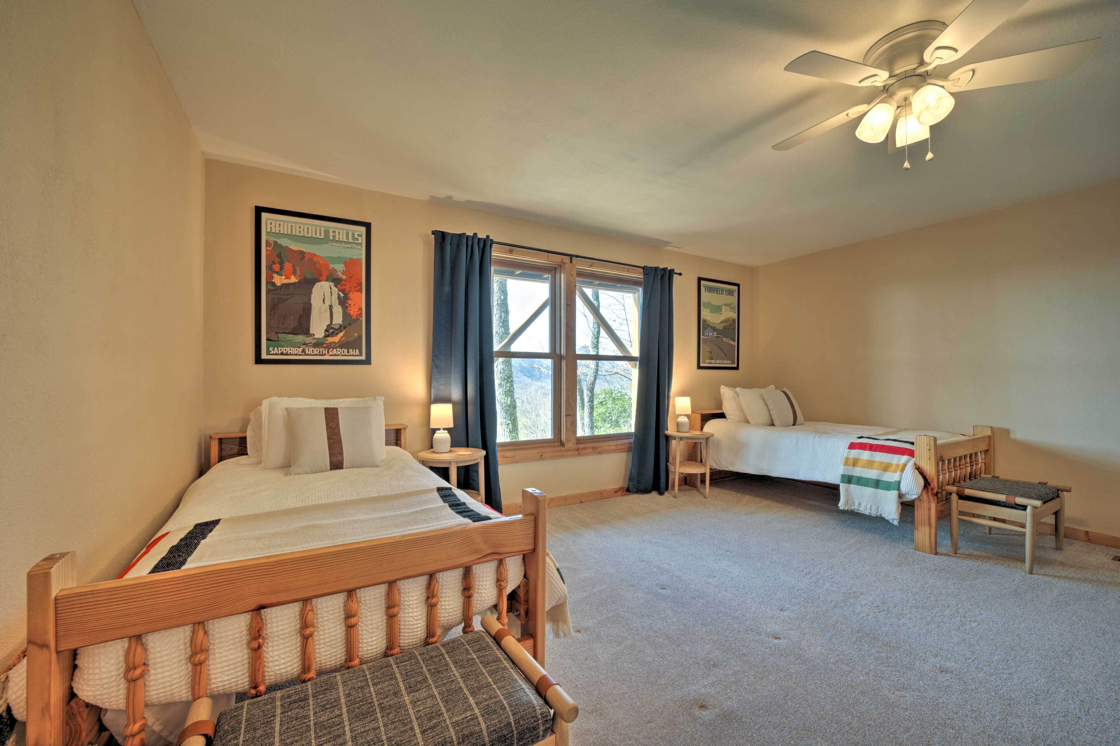 A bedroom with a bed, a chair, a bedside table, a nightstand, a window with curtains, a ceiling fan, and a poster on the wall.
