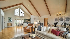 A spacious living area with a high ceiling, wooden beams, a large window, a fireplace, and a dining area with chairs and a table. - Sapphire 5BR Luxe: 5 Private Baths, Mtn Views (Sapphire)