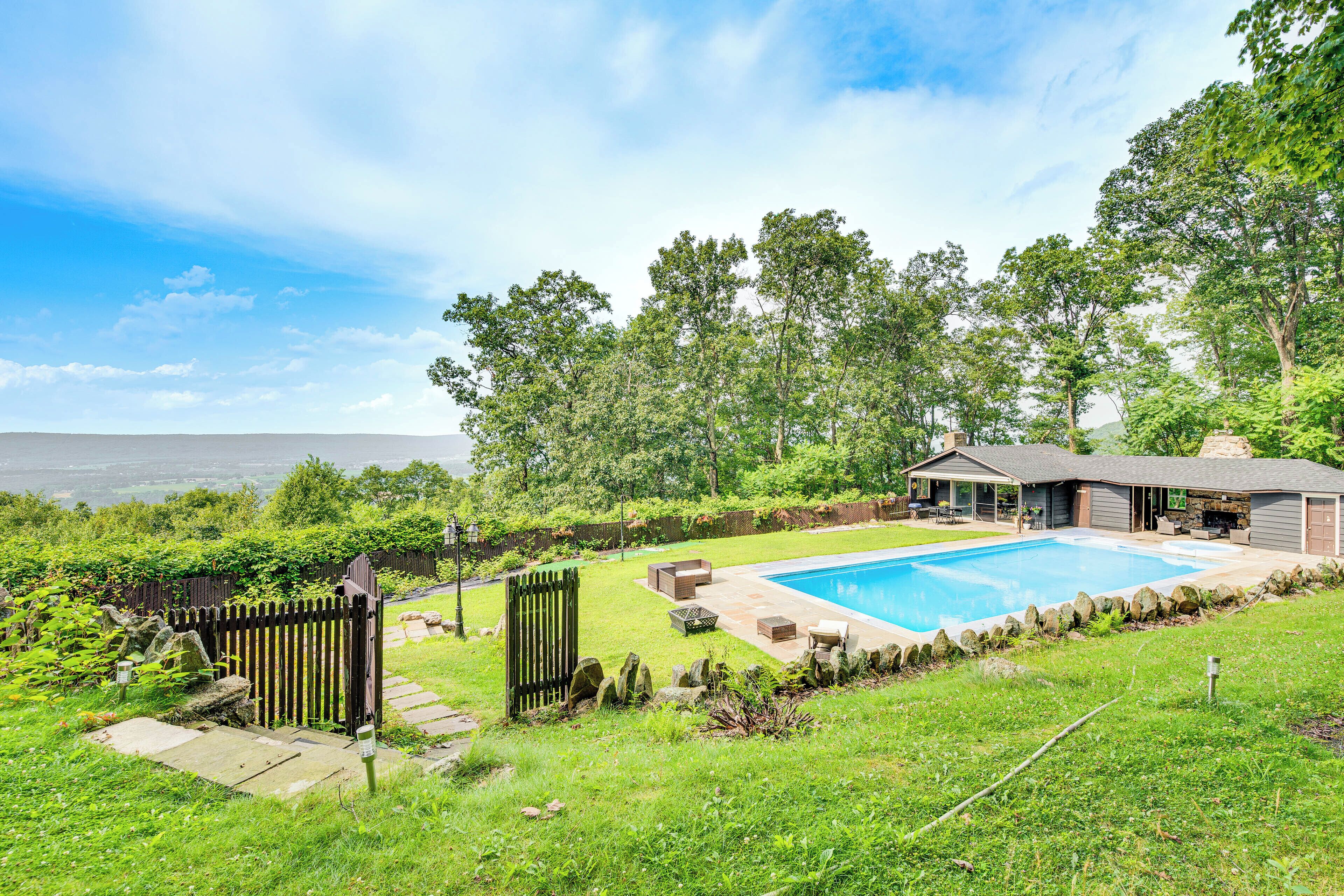 A backyard with a swimming pool, a patio with outdoor furniture, and a view of the surrounding landscape.