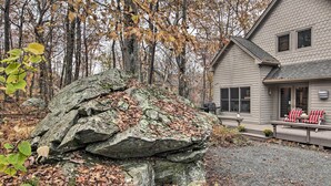 A house with a stone feature in front, a porch with striped chairs, and a forested background. - Wintergreen Resort Cabin: Near the Slopes! (Roseland)