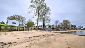 A sandy beach with a wooden fence, a white house, and trees in the background. - Waterfront Cottage w/ Private Beach + Deck! (Colonial Beach)