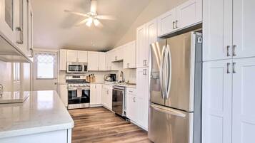 A modern kitchen with white cabinets, stainless steel appliances, and a wooden floor.