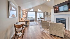 A spacious living room with a fireplace, a television mounted above it, and a dining area with a table and chairs. - Waterfront Cottage w/ Private Beach + Deck! (Colonial Beach)