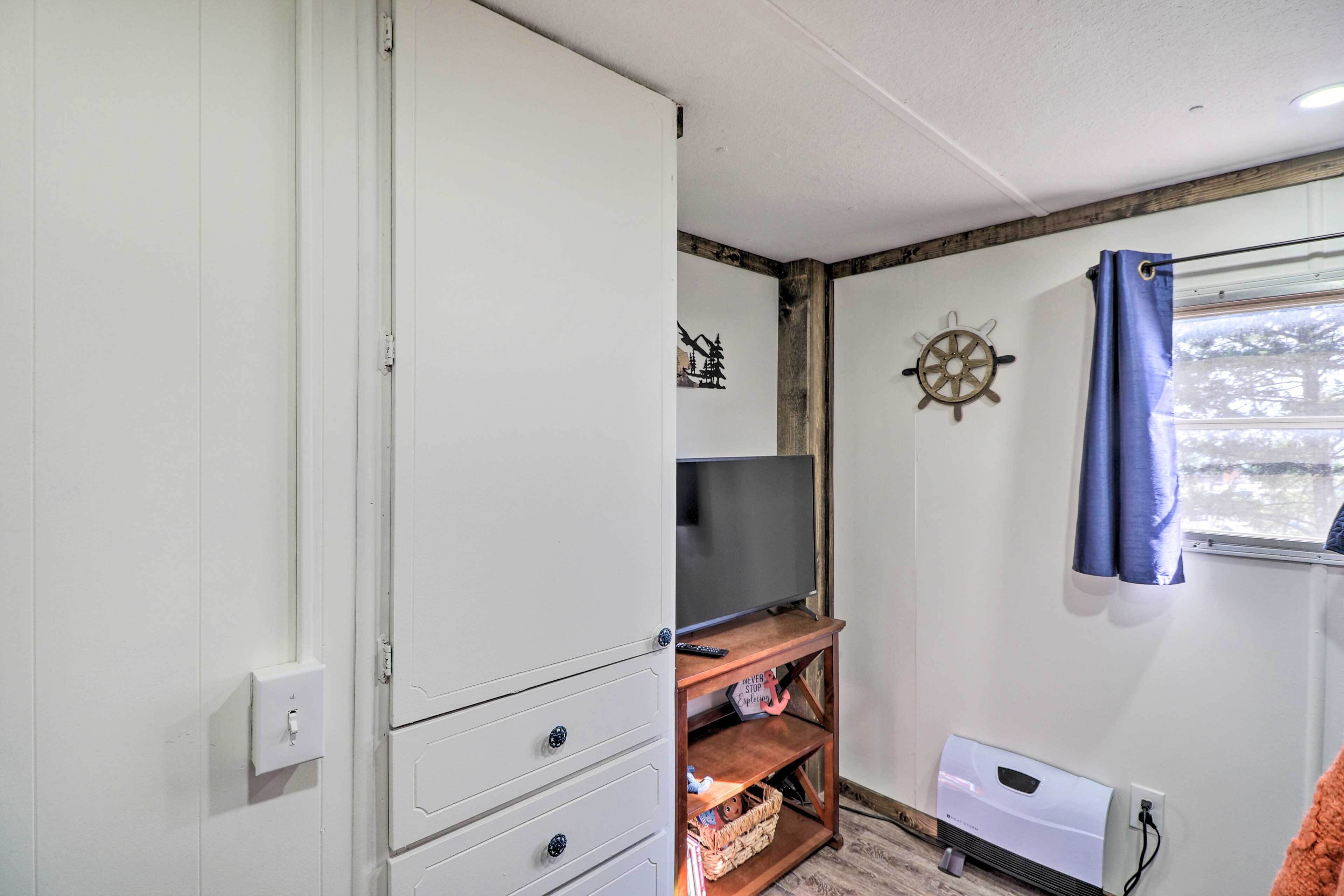 A room with a white wardrobe, a wooden TV stand, a ship's wheel decoration, and a window with blue curtains.