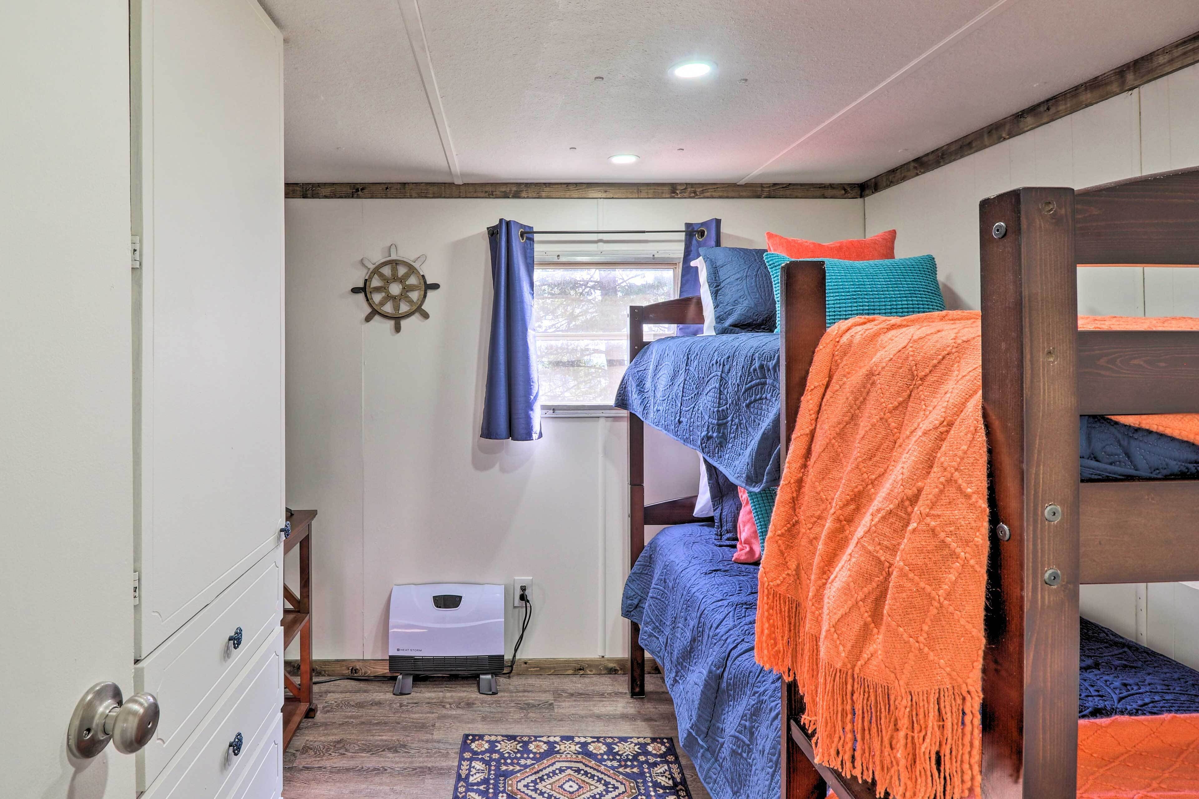 A compact room with bunk beds, a small window with curtains, a heater, and a decorative wall piece.