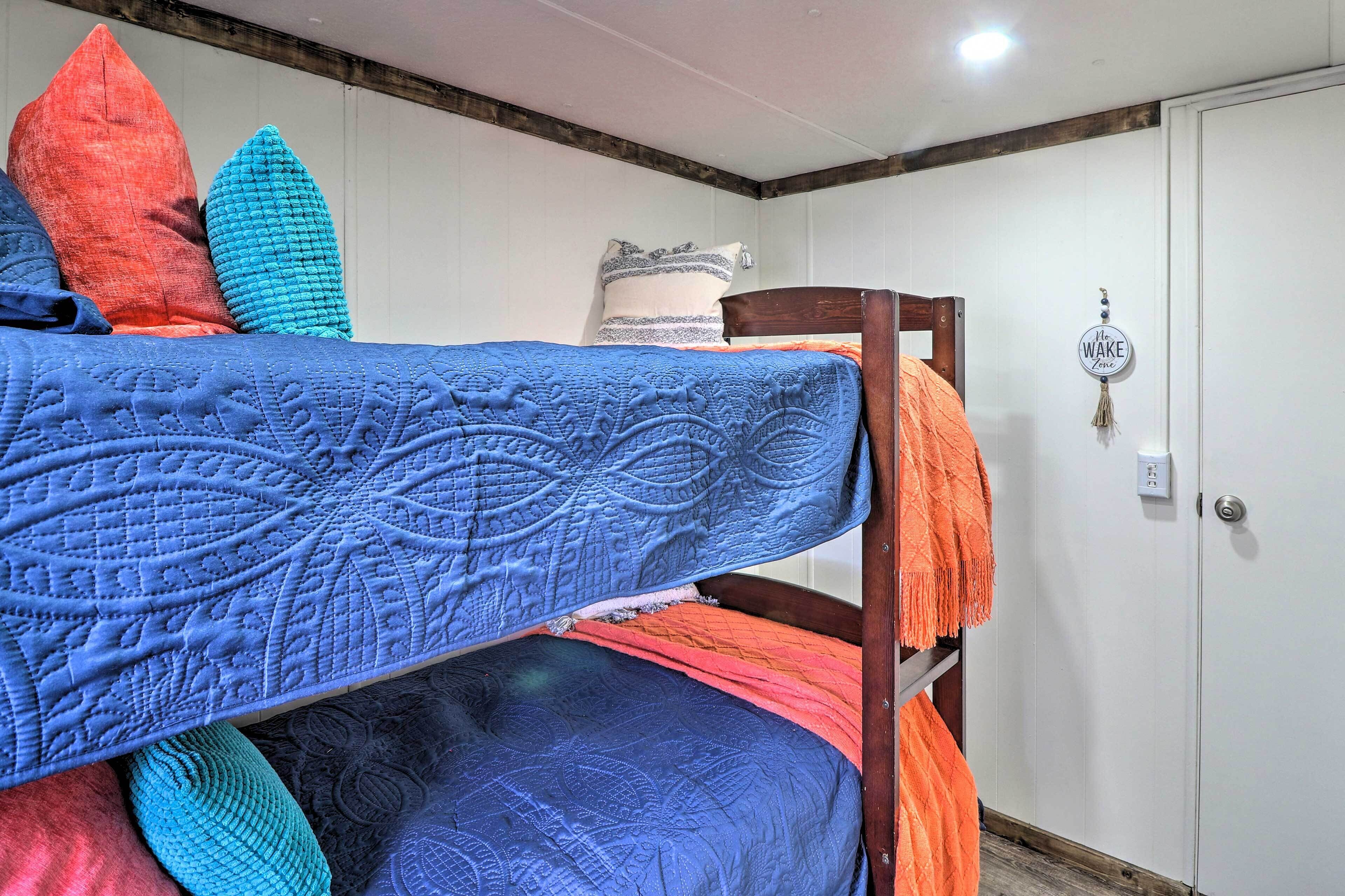 A bunk bed with a blue quilt, a wooden headboard, and a white door with a "Please Wake Me" sign.