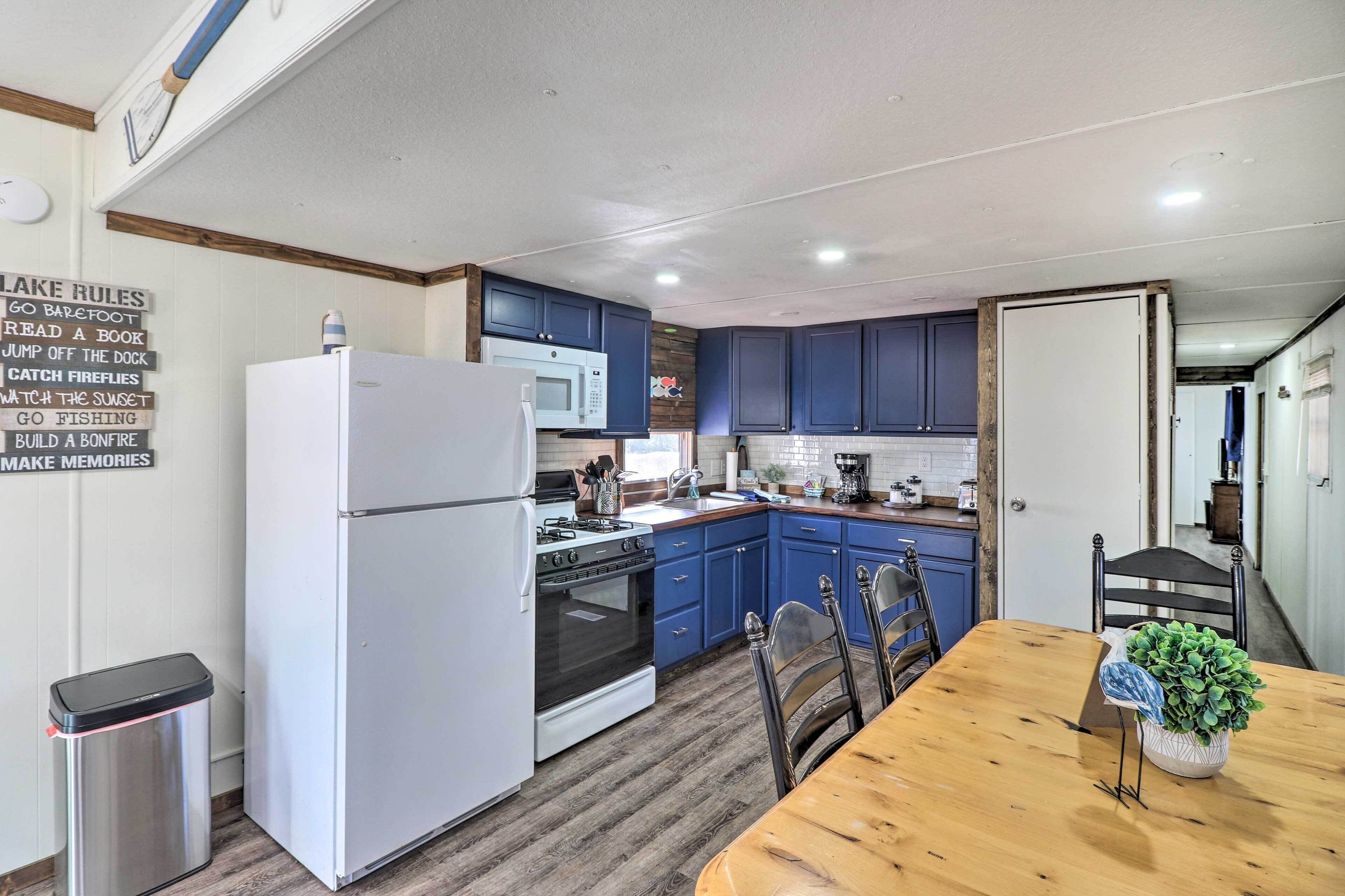 A modern kitchen with a refrigerator, stove, microwave, and sink. There is a wooden dining table with chairs and a potted plant.