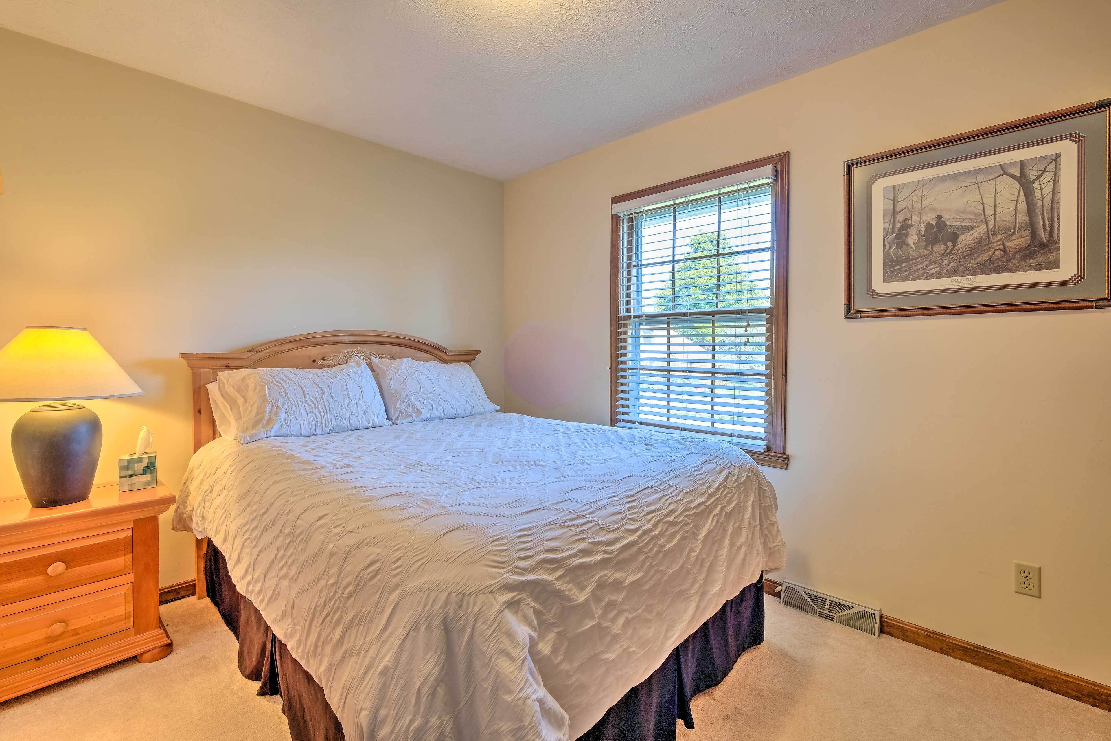 A neatly made bed with a white comforter and a wooden headboard, a bedside lamp, and a framed picture on the wall.