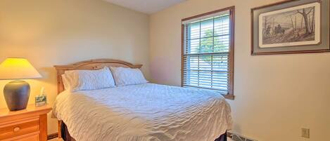 A neatly made bed with a white comforter and a wooden headboard, a bedside lamp, and a framed picture on the wall.