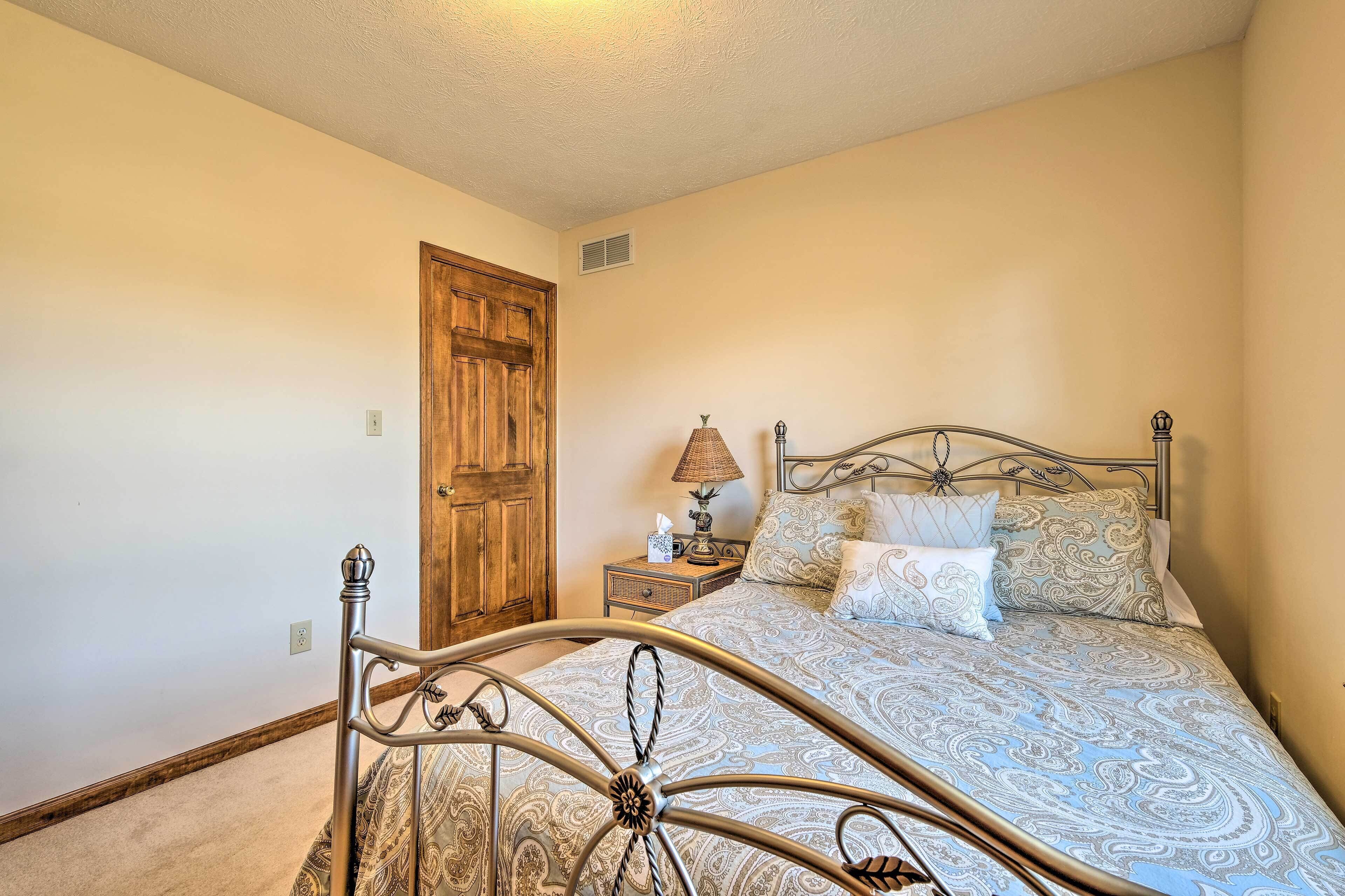 Une chambre à coucher avec un lit en métal, une porte en bois, une table de chevet avec une lampe et une couvre-lit à motifs.