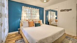 A bedroom with a large bed, a wooden floor, a blue accent wall, and a ceiling light fixture. - Renovated Eureka Springs Home - 1 Mi to Downtown! (Eureka Springs)