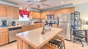 A kitchen with wooden cabinets, a central island, a refrigerator, a microwave, and a ceiling fan.