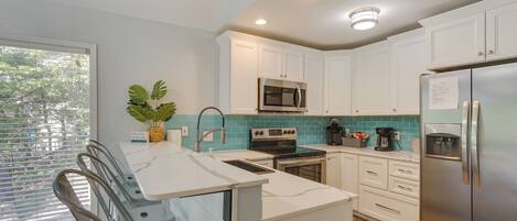 A modern kitchen with white cabinets, stainless steel appliances, and a window with blinds.
