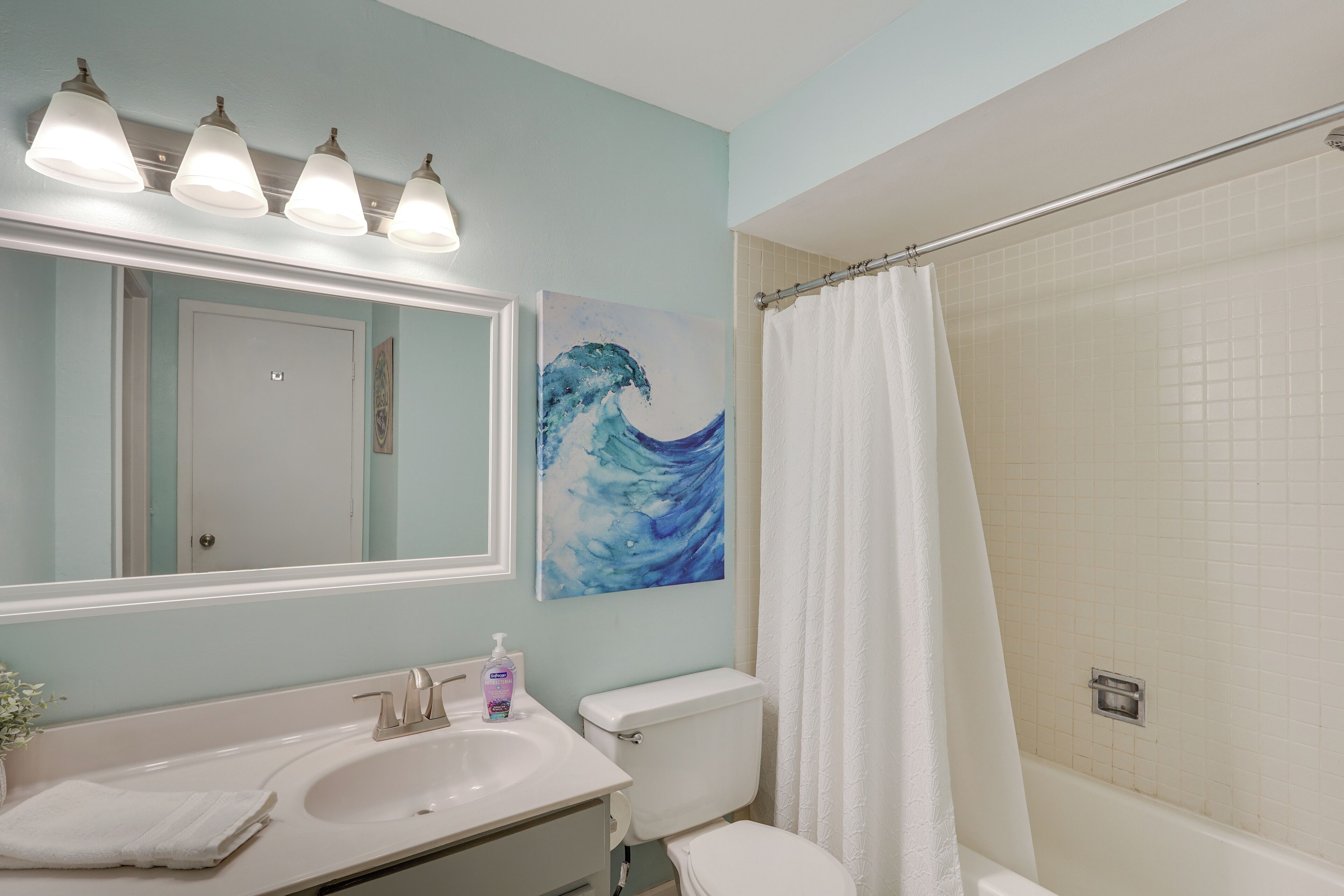 A bathroom with a sink, mirror, toilet, and shower curtain.