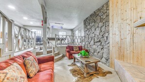 Un salon chaleureux avec un canapé rouge, une table basse en bois et un mur en pierre.