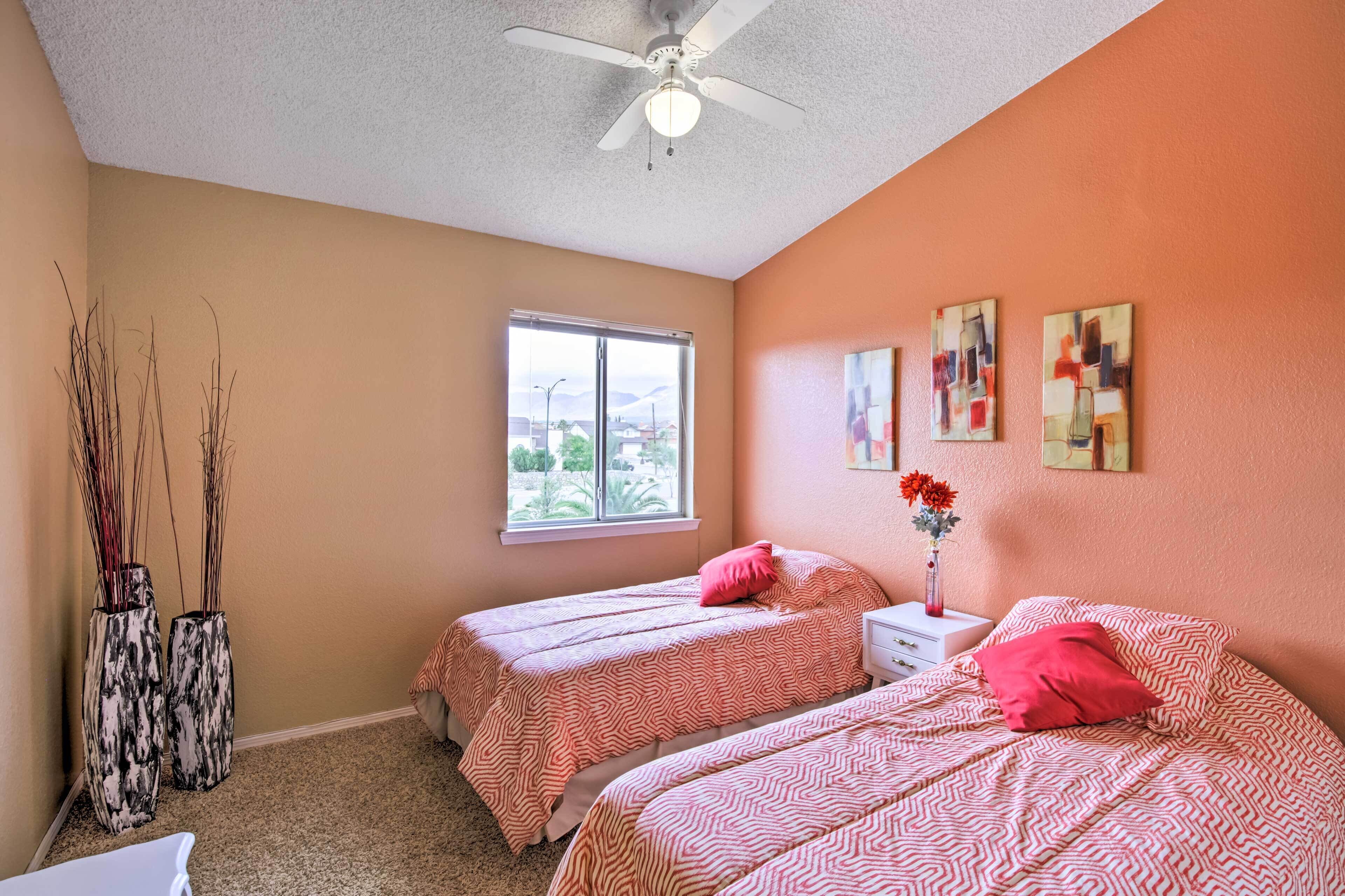 A bedroom with two beds, a ceiling fan, a window, and abstract wall art.