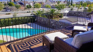 A pool area with a view of mountains, a patio with wicker furniture, and a stone wall.