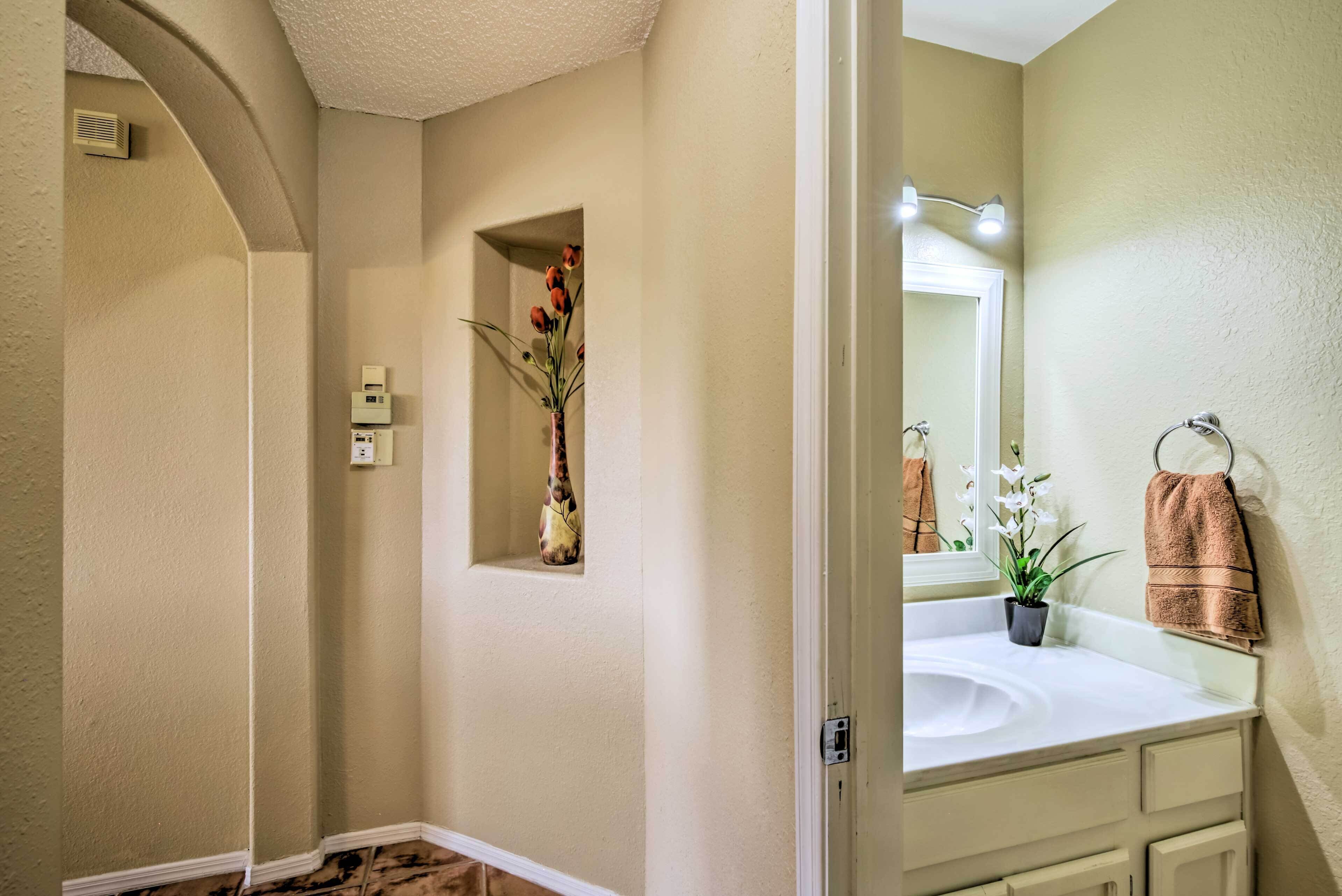 A bathroom with a white sink, a mirror, a towel rack, and a vase with flowers.