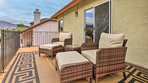 A balcony with wicker furniture and a patterned rug.