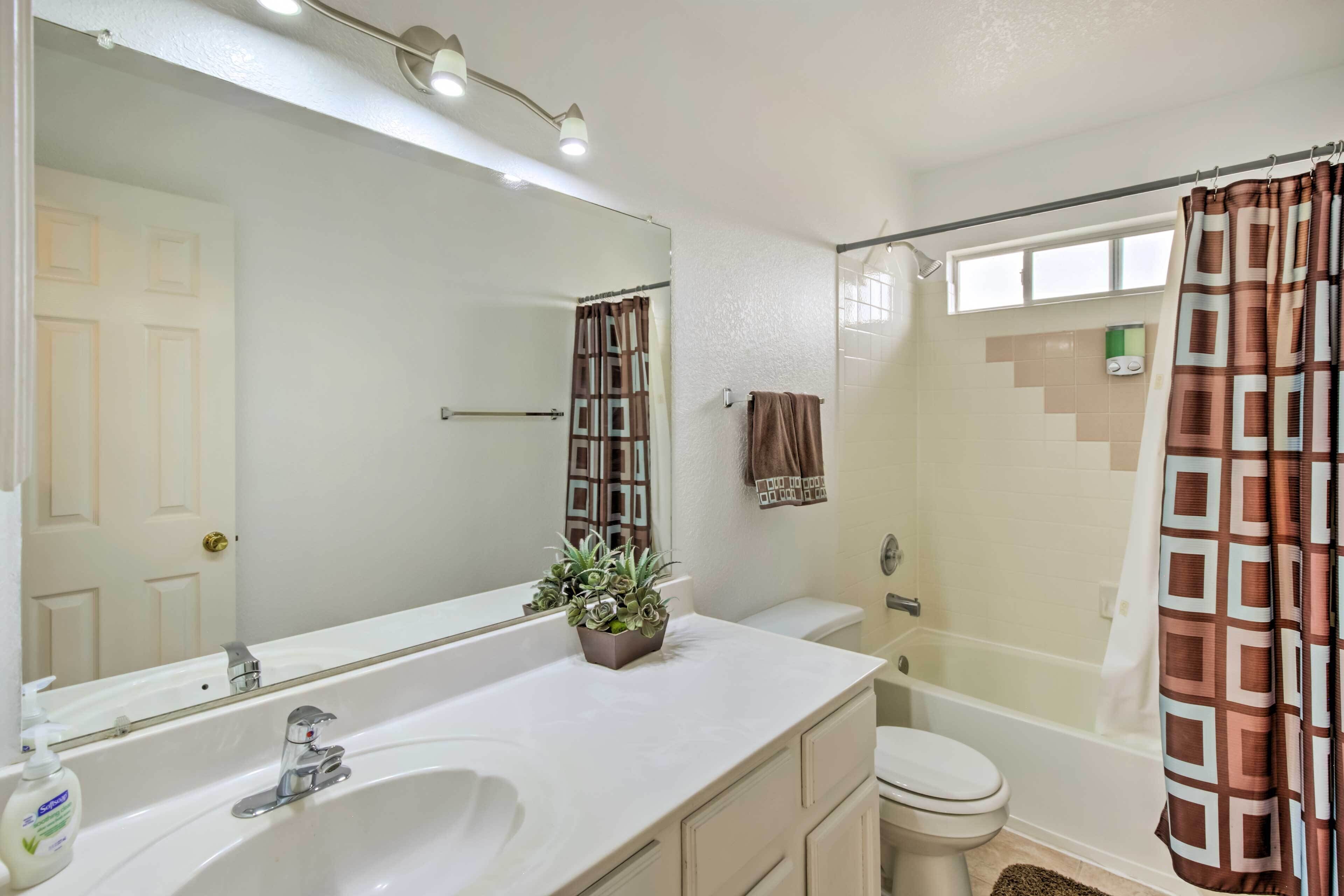 A bathroom with a white sink, a mirror, a toilet, and a shower with a patterned curtain.